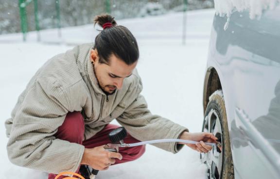 Eine Person prüft den Reifendruck eines Autos auf schneebedecktem Boden.