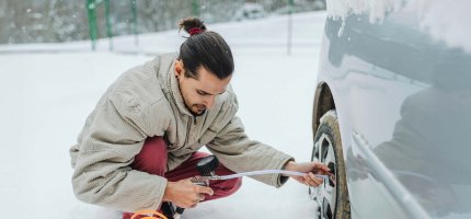 Eine Person prüft den Reifendruck eines Autos auf schneebedecktem Boden.