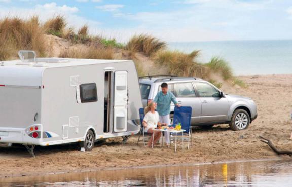 Familie mit Auto und Wohnwagen rastet am Strand.