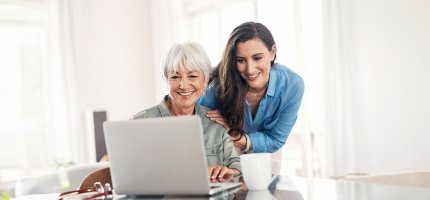 Eine alte und eine junge Frau schauen an einem Tisch auf einen Laptop.