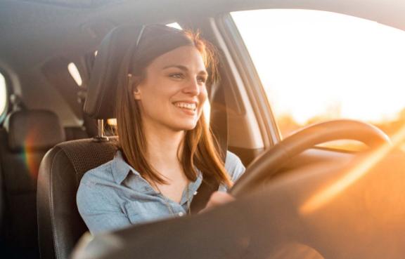 Eine Frau sitzt lächelnd im Auto und schaut in den Sonnenuntergang.