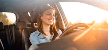 Eine Frau sitzt lächelnd im Auto und schaut in den Sonnenuntergang.