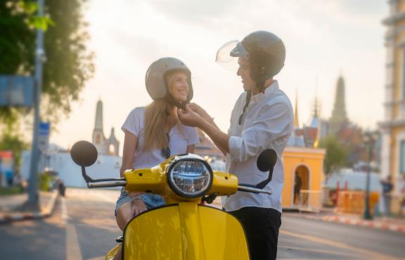 Ein Mann zieht einer Frau auf einem Motorroller einen Helm an.