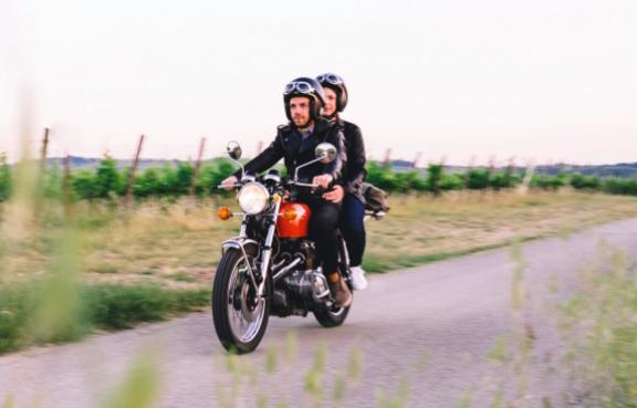 Ein Paar fährt mit einem alten Motorrad über einen Feldweg.