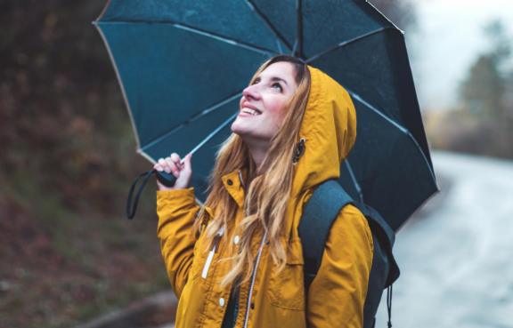 Frau mit gelber Regenjacke und schwarzem Schirm schaut nach oben.