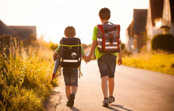 Zwei kleine Jungs mit Schulranzen gehen Hand in Hand durch ein Dorf.
