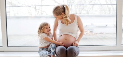 Kleines Mädchen fasst seiner Mutter an den schwangeren Bauch und lacht.