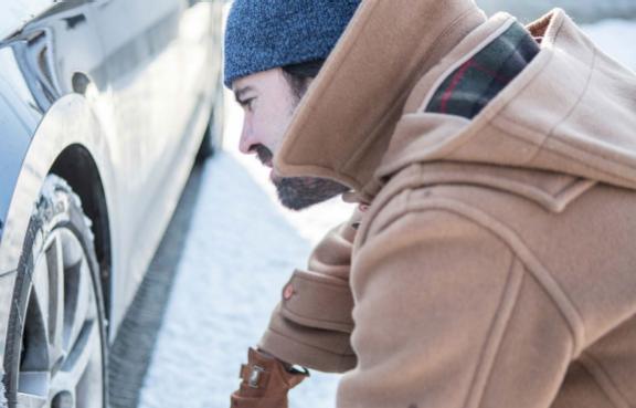 Eine Person trägt warme Kleidung und überprüft den Reifen eines Autos im Schnee.