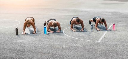 Vier Sportler machen die Planke auf Yogamatten auf einem Sportplatz.