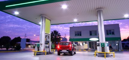 Rotes Auto fährt in der Abenddämmerung an eine Zapfsäule einer Tankstelle.