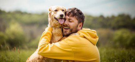 Ein Mann knuddelt draußen seinen Hund.