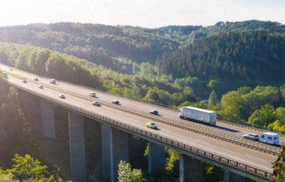 Eine befahrene Autobahnbrücke neben Wäldern von oben.