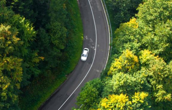 Blick von oben auf ein fahrendes Auto auf einer Landstraße durch den Wald.