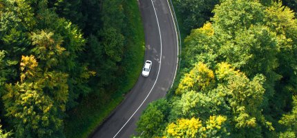 Blick von oben auf ein fahrendes Auto auf einer Landstraße durch den Wald.