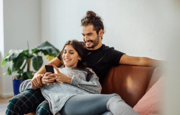 Mann und Frau kuscheln auf einer Couch und schauen auf ein Handy.