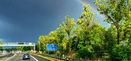 Dunkle Wolken mit einem Regenbogen über einer Autobahn