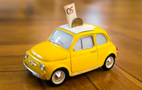 Eine Spardose in Form eines kleinen gelben Fiat 500 mit Geldschein und einer Münze im Schlitz.