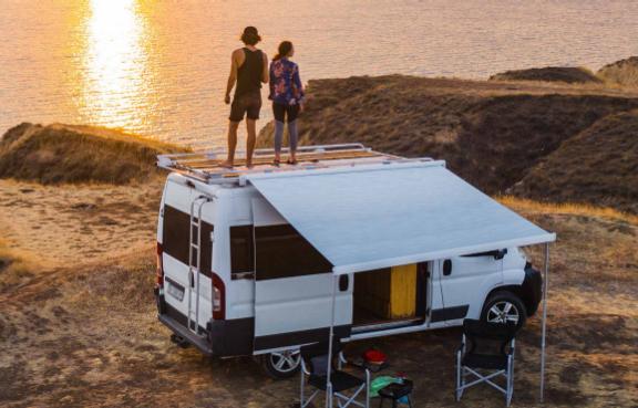 Pärchen steht auf dem Dach ihres Campers am Meer.