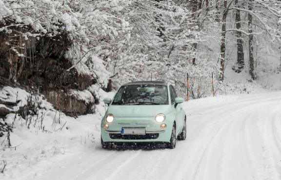 Ein Kleinwagen fährt im Wald über eine verschneite Straße.
