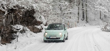 Ein Kleinwagen fährt im Wald über eine verschneite Straße.