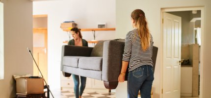 Zwei Frauen tragen ein Sofa in eine Wohnung.