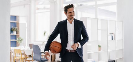 Mann im Anzug mit Basketball unter dem Arm in einer Wohnung.