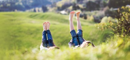 Zwei Kinder liegen rücklings im Gras und strecken ihre Beine in den Himmel.