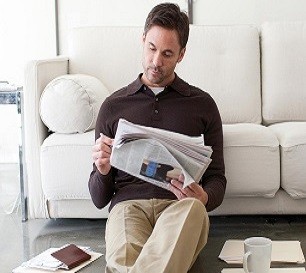 Ein Mann sitzt vor seiner Couch und liest die Tageszeitung.
