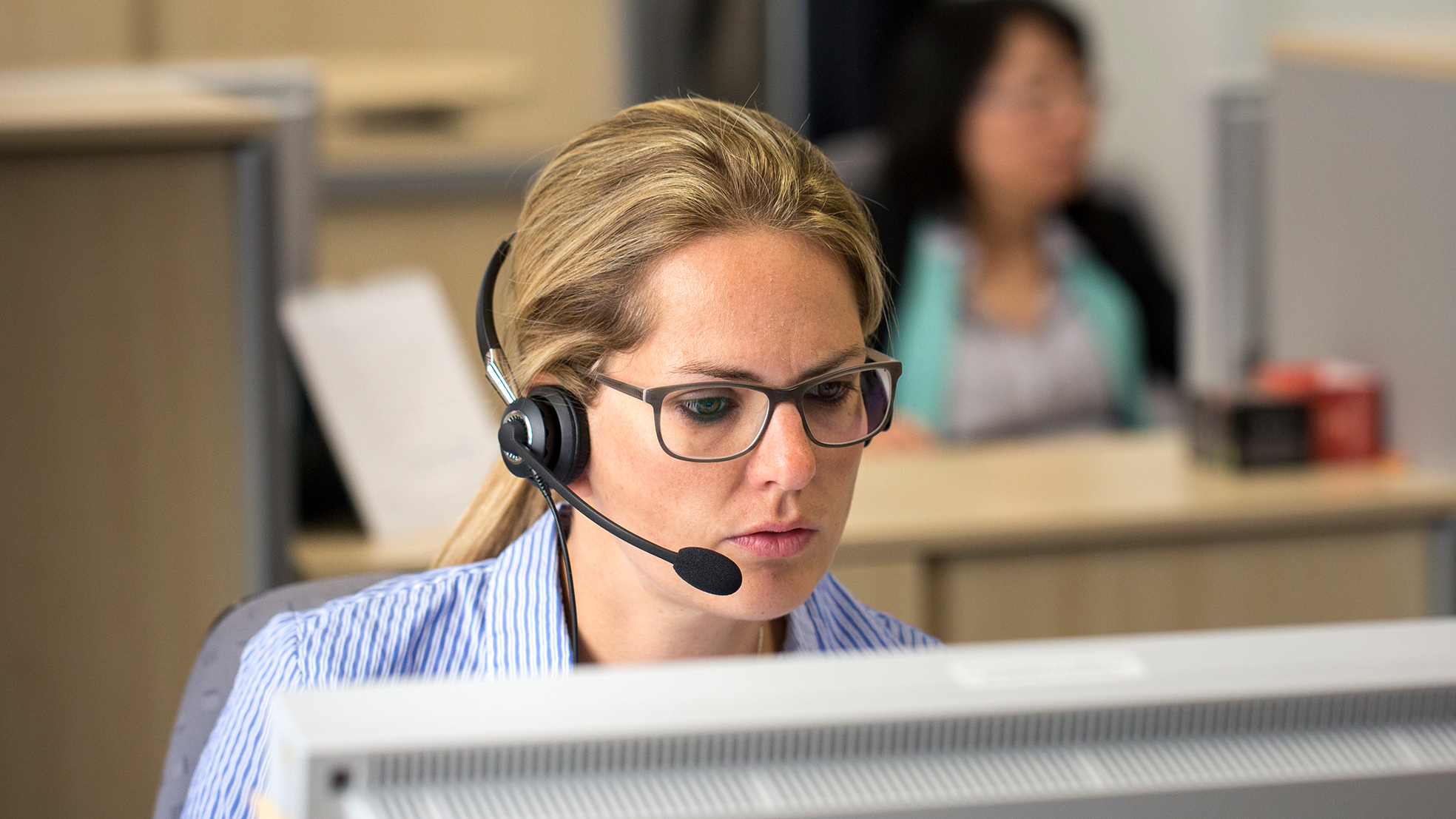 Eine Frau mit Brille sitzt am Computer und hat ein Headset auf dem Kopf.