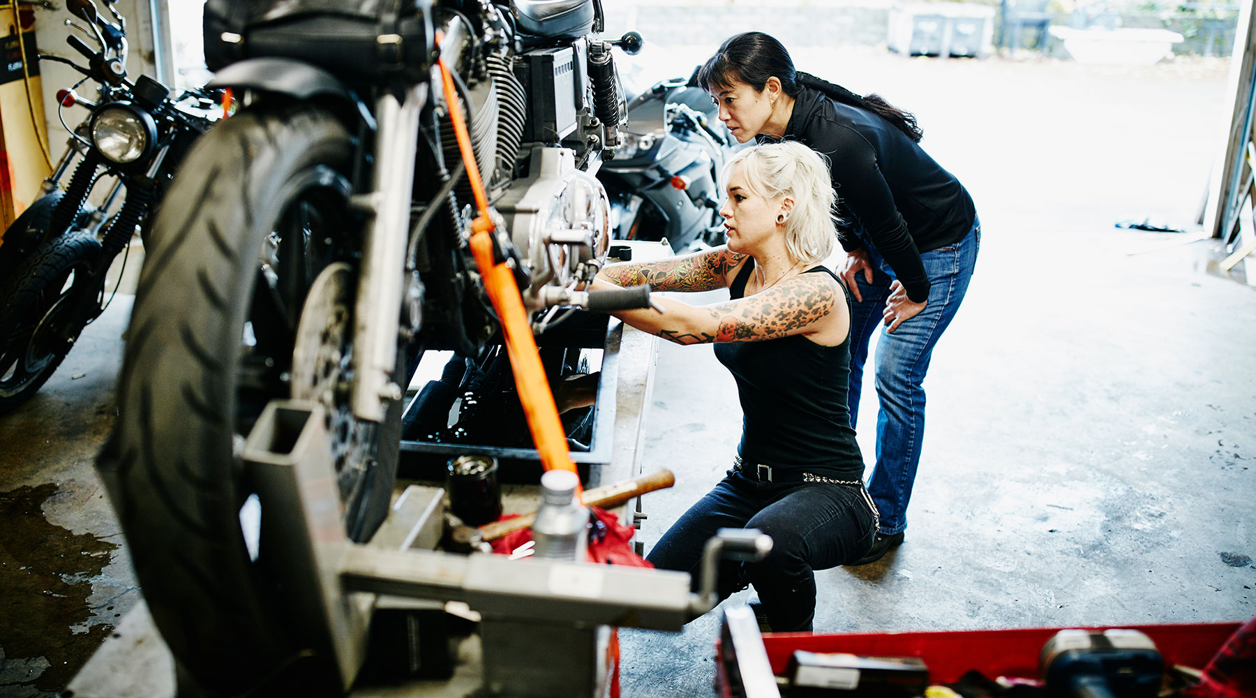 Zwei Frauen schrauben an einem Motorrad in einer Garage.