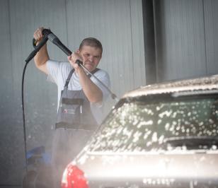 Ein Werkstattmitarbeiter wäscht ein Auto mit einem Dampfstrahler.