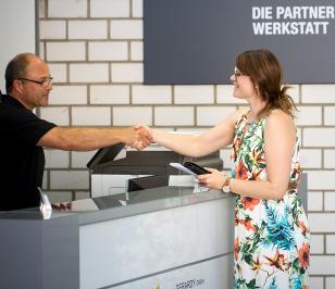 Partnerwerkstatt-Mitarbeiter gibt einer Kundin die Hand