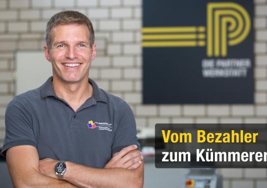 Porträt eines Partnerwerkstatt-Mitarbeiters in einer Werkstatt. Im Hintergrund ist das Logo der Partnerwerkstatt zusehen.