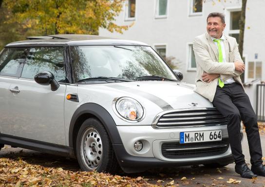 Ein Kunde der HUK-COBURG lehnt an seinem Auto, einem Mini Cooper.