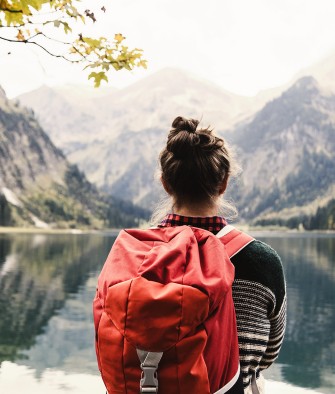 Junge Frau mit Rucksack schaut auf einen Bergsee mit Alpenpanorama.