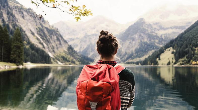 Junge Frau mit Rucksack schaut auf einen Bergsee mit Alpenpanorama.