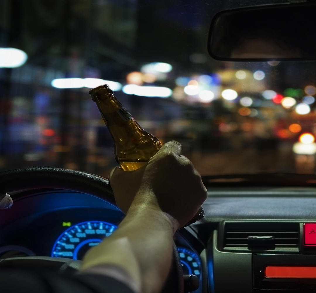 Mann hält während des Autofahrens eine Flasche Bier in der rechten Hand.