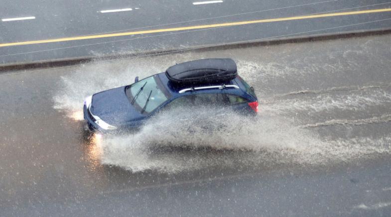 Ein Auto fährt durch das Wasser einer überschwemmten Straße.