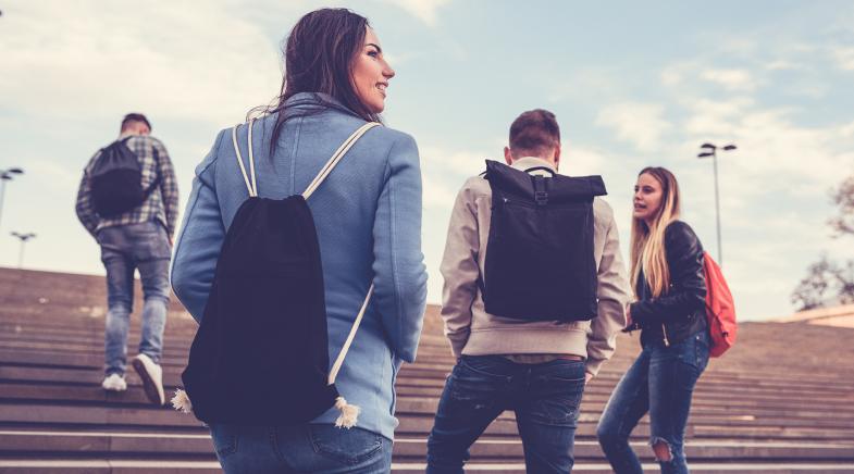 Zwei männliche und zwei weibliche Studenten mit Rucksäcken gehen draußen eine Treppe hoch und unterhalten sich.