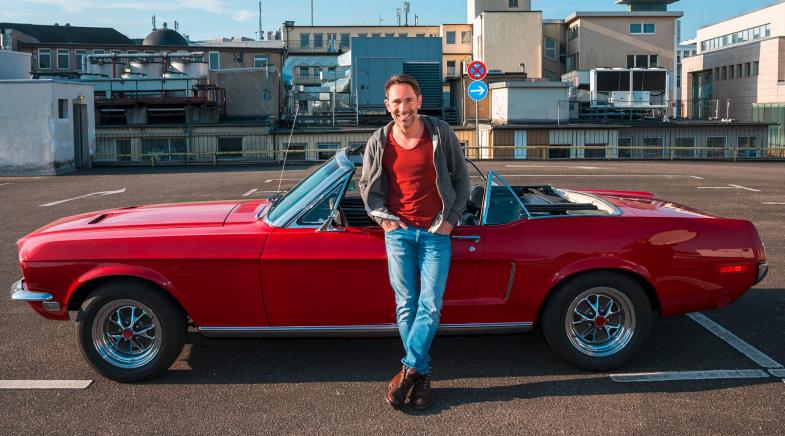 Mann lehnt an einem alten Ford Mustang