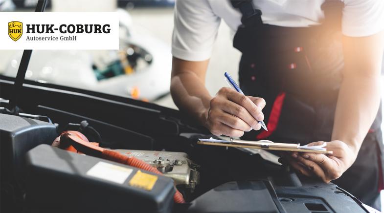 Mechaniker füllt vor offener Motorhaube ein Dokument auf einem Klemmbrett aus.