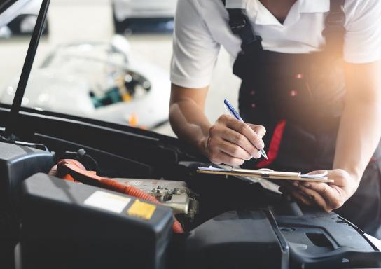 Mechaniker geht an einem Auto eine Checkliste durch.