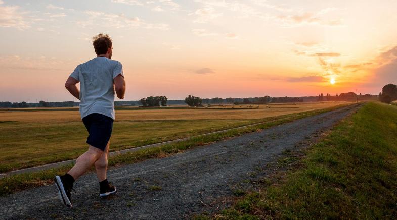 Jogger auf einem Feldweg bei Sonnenuntergang.