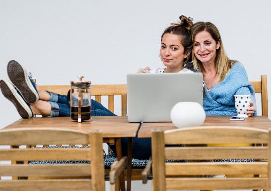 Mutter und Tochter sitzen am Tisch, trinken Kaffee und schauen auf einen Laptop.