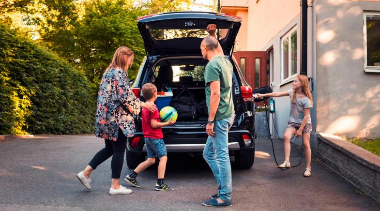 Familie lädt und belädt ein Elektroauto vor ihrem Haus.