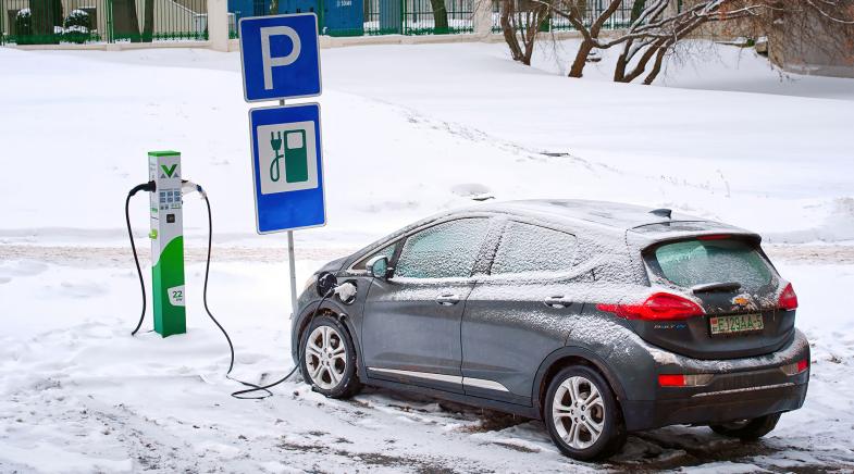 E-Auto steht im Winter vor einer verschneiten Ladesäule und lädt.