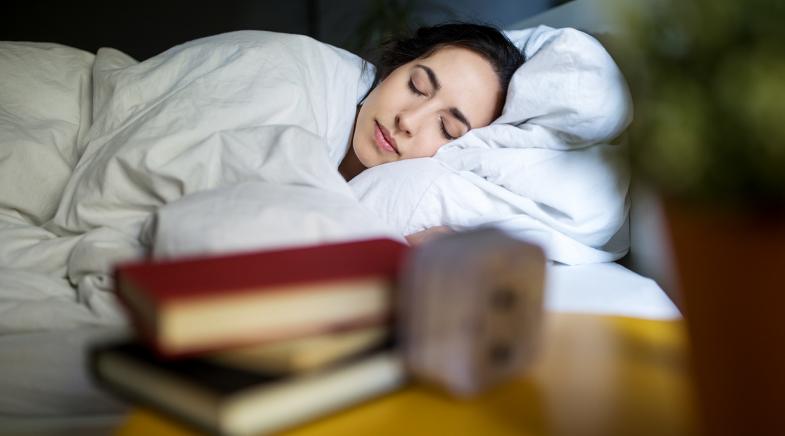 Frau mit geschlossenen Augen im Bett unter einer weißen Decke.