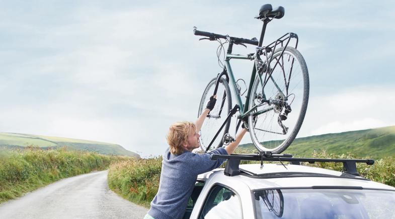 Mann montiert Fahrrad auf dem Fahrradträger auf seinem Autodach.