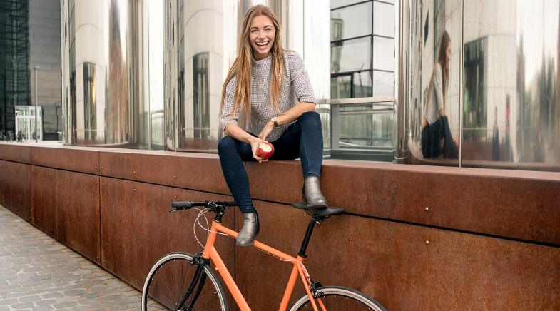 Frau sitzt auf rostiger Mauer an der ihr Fahrrad lehnt.