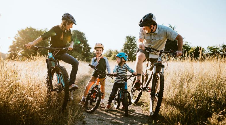 Eine junge Familie hält während ihrer Fahrradtour auf einem Feldweg.